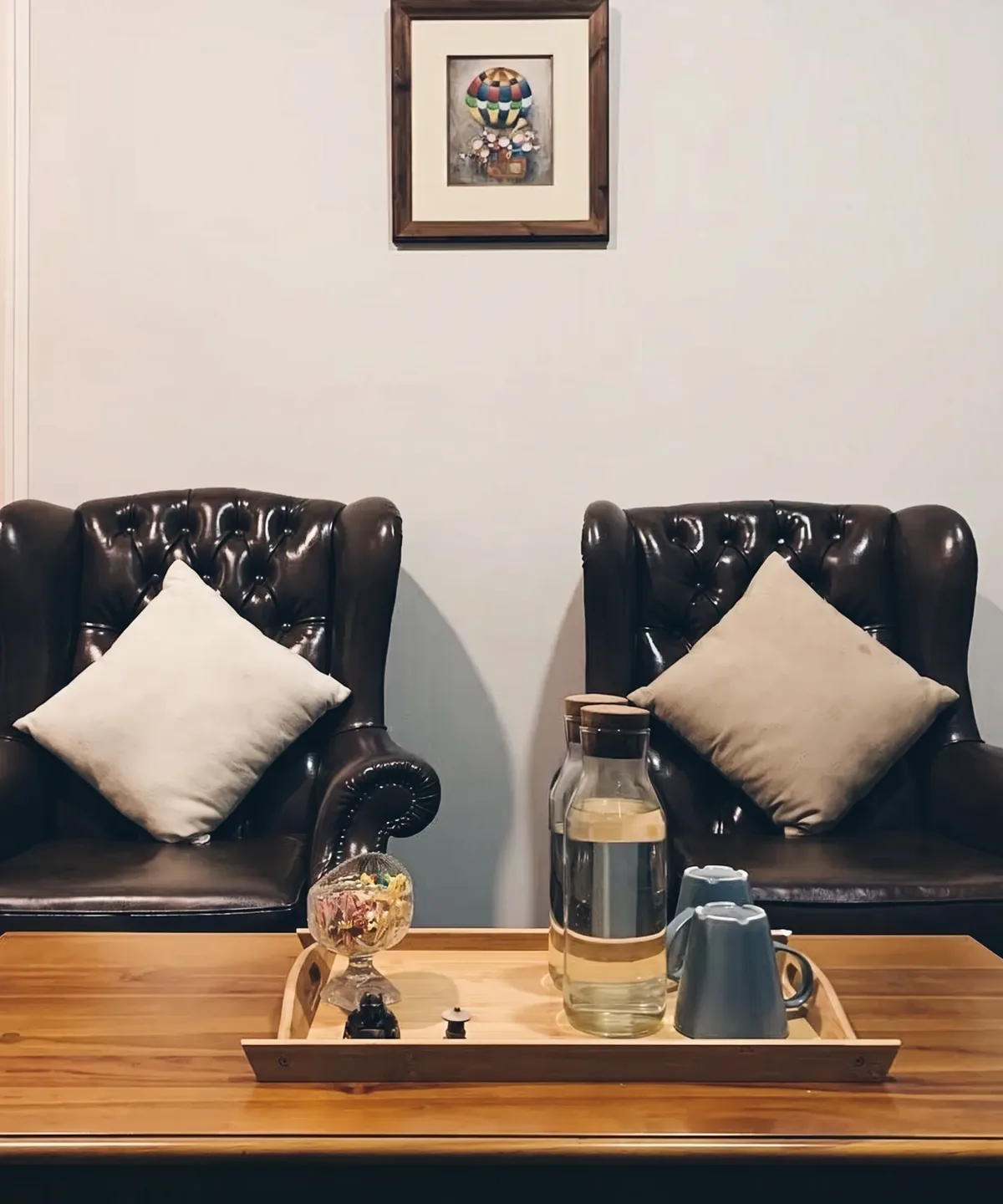 A consultation room at The Mind Faculty — two leather wingback chairs either side of a wooden table set with a water carafe, framed artwork above